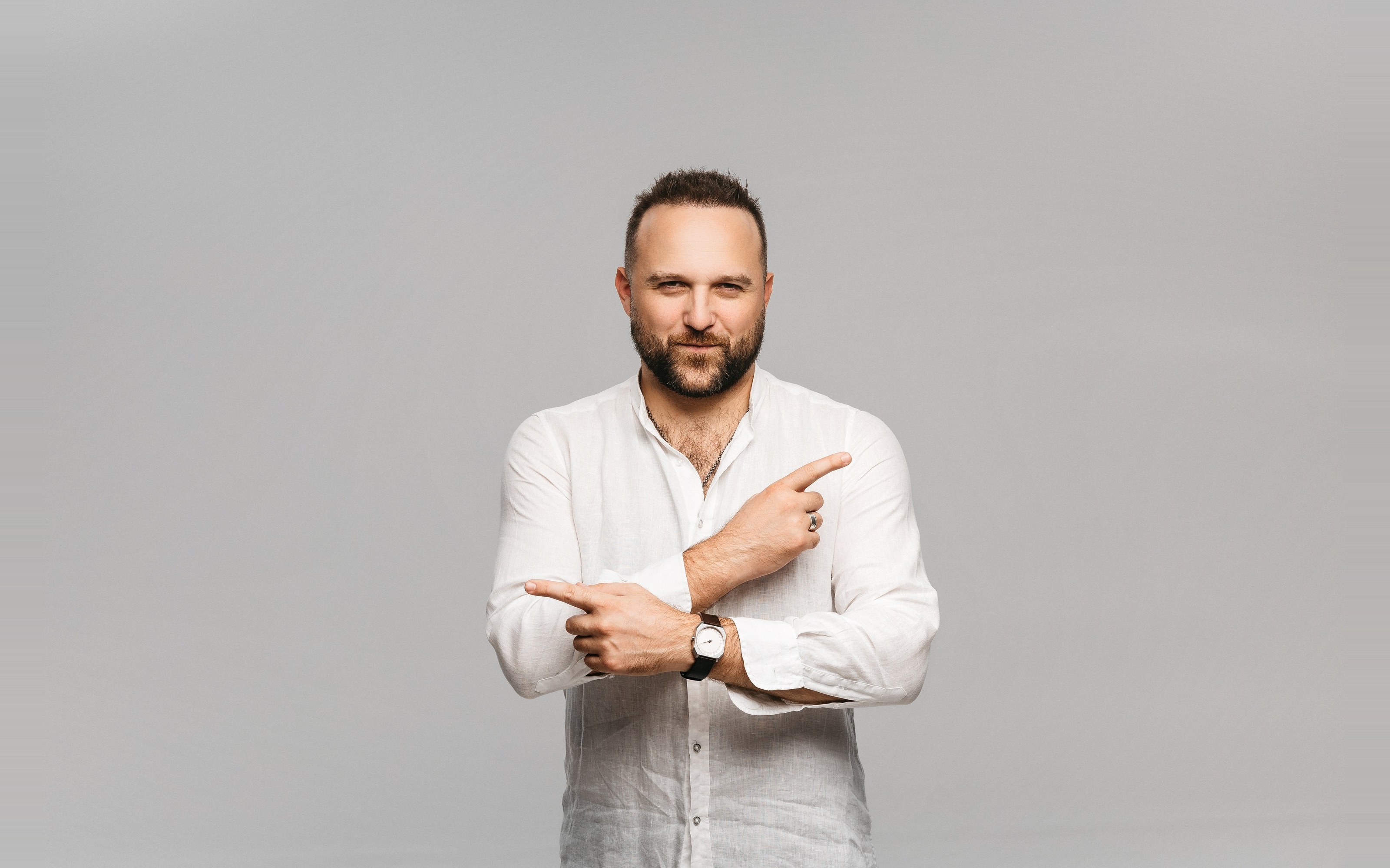 Dimitry Los in a white linen shirt, arms crossed, pointing left and right